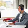 A young man wearing a gaming headset is sitting at a desk and using a computer. Produktbild-Vorschau