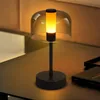 A modern black table lamp with a glass shade and a warm yellow light is placed on a dark wooden table. Anteprima dell’immagine prodotto
