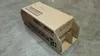 A cardboard box for a Kyocera toner cartridge is shown on a concrete floor. Podgląd zdjęcia produktu