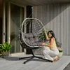 A woman kneels next to a hanging egg chair on a wooden deck. Produktbild-Vorschau
