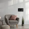 A weather station is mounted on a wall above a gray armchair with a pink cushion. A potted plant is to the right of the chair. Produktbild-Vorschau