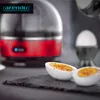 A red egg cooker with a clear lid, next to some sliced boiled eggs and a whole boiled egg in a holder. Anteprima dell’immagine prodotto