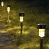 A line of solar garden lights illuminating a grassy area next to a paved path at dusk. Anteprima dell’immagine prodotto