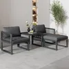 An outdoor seating set with two chairs, a side table, and an ottoman, arranged on a light gray floor against a light gray wall with a built-in shelf unit. Produktbild-Vorschau