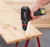A hand holding a cordless drill and screwing a screw into a wooden plank. Produktbild-Vorschau