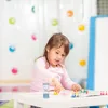 A young girl plays a board game at a table with colorful game pieces and an hourglass timer. Voir les images du produit