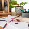 A person's hand is decorating a white t-shirt with fabric markers, with a pot of plants and a wooden easel in the background. Produktbild-Vorschau