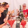 People gathered around a table with a small Christmas tree, wearing festive accessories. Produktbild-Vorschau