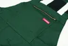 A close-up view of a green pair of overalls, showing a pocket with a zipper and a red brand tag. Náhled obrázku produktu