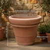 A terracotta pot with dimensions and volume indicated by text overlays, placed outdoors against a stone wall and foliage. Produktbild-Vorschau