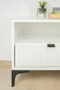 A close-up of a white cabinet with a black handle and black legs, placed on a light wooden floor. Podgląd zdjęcia produktu