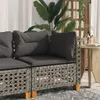 A close-up of a gray poly rattan corner sofa with dark gray cushions, set in an outdoor or indoor setting with plants and a wooden table. Produktbild-Vorschau