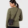 A woman wearing a green sweater and a black crossbody bag. Produktbild-Vorschau