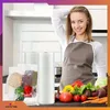 A woman in an apron in a kitchen, with vacuum sealing rolls and fresh produce. Podgląd zdjęcia produktu
