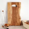 A wooden cutting board is displayed on a table with a bottle and bread in the background. Náhľad obrázku produktu