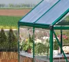 A close-up view of a green greenhouse filled with various potted plants, set in an outdoor garden environment. Podgląd zdjęcia produktu