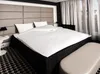 A hotel room bed with white bedding and a padded headboard. Produktbild-Vorschau