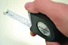 A hand holding a black tape measure with the tape extended. Anteprima dell’immagine prodotto