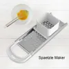 A spaetzle maker with a bowl of whisked eggs and a whisk are placed on a white wooden surface. Produktbild-Vorschau