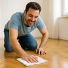 A man is kneeling on a wooden floor, cleaning it with a white cloth. Produktbild-Vorschau