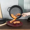 A hand is holding a cast iron pan with ribs being poured onto a red plate. Náhled obrázku produktu