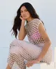 A woman is sitting and posing for a photo, wearing a crocheted dress. Produktbild-Vorschau