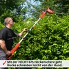 A man is using a long-reach hedge trimmer to trim a large hedge outdoors. Produktbild-Vorschau