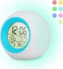 A digital alarm clock with a blue rim and a digital display showing the time, day, month, date, and temperature. The clock is illuminated with a soft glow. Produktbild-Vorschau