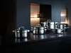 A set of stainless steel pots and pans arranged on a dark countertop in a modern kitchen setting. Produktbild-Vorschau