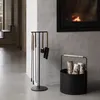 A fireplace set and log basket are placed on a concrete floor next to a fireplace. Anteprima dell’immagine prodotto