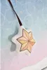 A close-up of a plush star ornament hanging from a dark ribbon against a background with a geometric pattern in shades of blue and pink. Produktbild-Vorschau