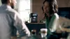 A couple is in a modern kitchen, with a coffee machine on the counter and coffee cups on a table. Produktbild-Vorschau