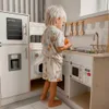 A young child is playing with a wooden toy kitchen. Podgląd zdjęcia produktu