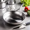 A stainless steel frying pan is shown on a gray countertop, with other cookware, peppercorns, and vegetables in the background. Voir les images du produit