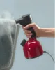 A hand holding a red and black handheld garment steamer, with steam rising and a gray fabric object in the foreground. Anteprima dell’immagine prodotto