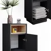 A close-up view of a black cabinet with an open door and a wooden shelf inside, displaying two bottles. Another cabinet is visible in the background, stacked with folded towels. Náhled obrázku produktu