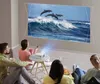 A group of people are watching a movie projected onto a wall from a mini projector. Produktbild-Vorschau