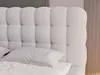 A close-up view of a white bouclé fabric headboard with tufted buttons, with a white pillow resting on the bed. Produktbild-Vorschau