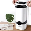 A person's hands are shown placing the top of a white humidifier onto its base, with a green monstera leaf in a vase on a wooden table in the foreground. Voir les images du produit