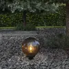 A decorative globe light sits on a gravel path in a garden at dusk. Produktbild-Vorschau