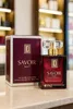 A perfume bottle and its box are displayed on a marble surface with shelves of other products in the background. Produktbild-Vorschau