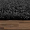A close-up view of a dark gray shaggy rug placed on a wooden floor. Produktbild-Vorschau