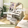 A white vanity table with a lighted mirror, drawers, and a stool, set up in a bedroom next to a bed and a plant. Voir les images du produit