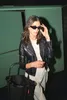A woman wearing a black leather jacket and sunglasses adjusts her sunglasses while holding a black mesh shopping bag. Voir les images du produit