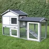 A wooden rabbit hutch with a gray roof and frame, and white walls, sits on a green lawn in front of a dense green hedge. Produktbild-Vorschau