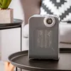 A white and gray Camry heater is placed on a black side table next to a chair. Voir les images du produit