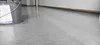 A roll of protective floor covering is shown in a room with a concrete floor and white walls. Produktbild-Vorschau