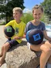 Two children sitting on a rock, holding round objects. Produktbild-Vorschau