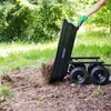 A person is using a black garden cart to dump soil in a grassy area. Náhled obrázku produktu