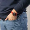 A person's wrist wearing a red watch, with their hand in their jeans pocket. Produktbild-Vorschau